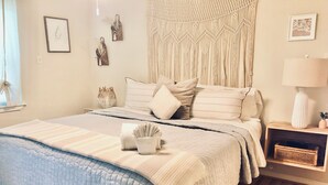 Un dormitorio ordenado con cama, mesitas de noche y un tapiz de macramé en la pared.