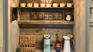 Una exhibición de café con un cartel que dice 'COFFEE', una cafetera, una botella de jarabe Torani y una cesta de granos de café.