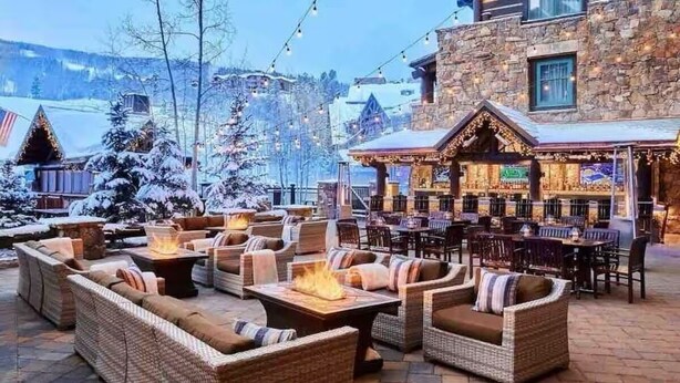 An outdoor seating area with wicker furniture and fire pits, a stone building with a bar, and snow-covered trees. - Ritz-Carlton Beaver Creek -- LUXURIOUS-2BR,2Bath, SLOPESIDE & inside hotel (Beaver Creek)