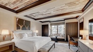 A spacious bedroom with a large bed, a bench, a desk, and a window overlooking a deck. - Ritz-Carlton Beaver Creek -- LUXURIOUS-2BR,2Bath, SLOPESIDE & inside hotel (Beaver Creek)