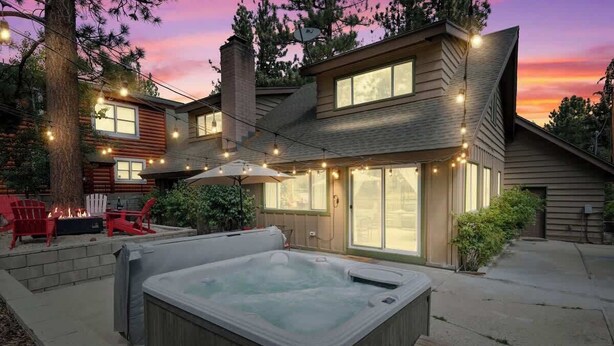 A modern house with a hot tub, outdoor seating, and string lights.