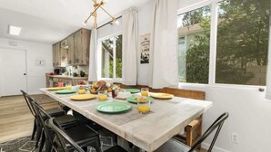 A modern kitchen with wooden cabinets, a dining table set for four, and a large window offering a view of trees.