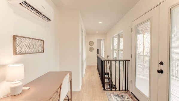 A hallway with a desk, chair, and lamp, leading to a staircase with a railing.