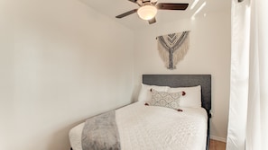 Un lit bien fait, avec une tête de lit grise, un plaid à motifs et une décoration murale au-dessus.
