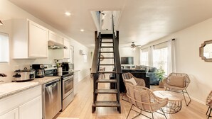 A modern kitchen with stainless steel appliances, a wooden ladder, wicker furniture, and a dining area with a view of the living room.