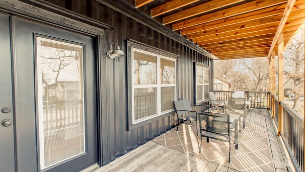 A covered deck with outdoor furniture and large windows.