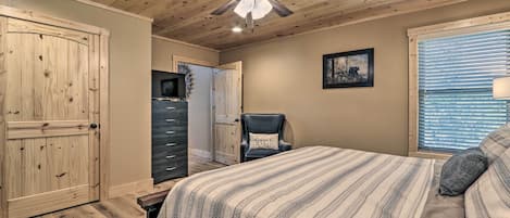Une chambre à coucher comprenant un lit, un ventilateur de plafond, une commode, une chaise et une fenêtre avec des stores.