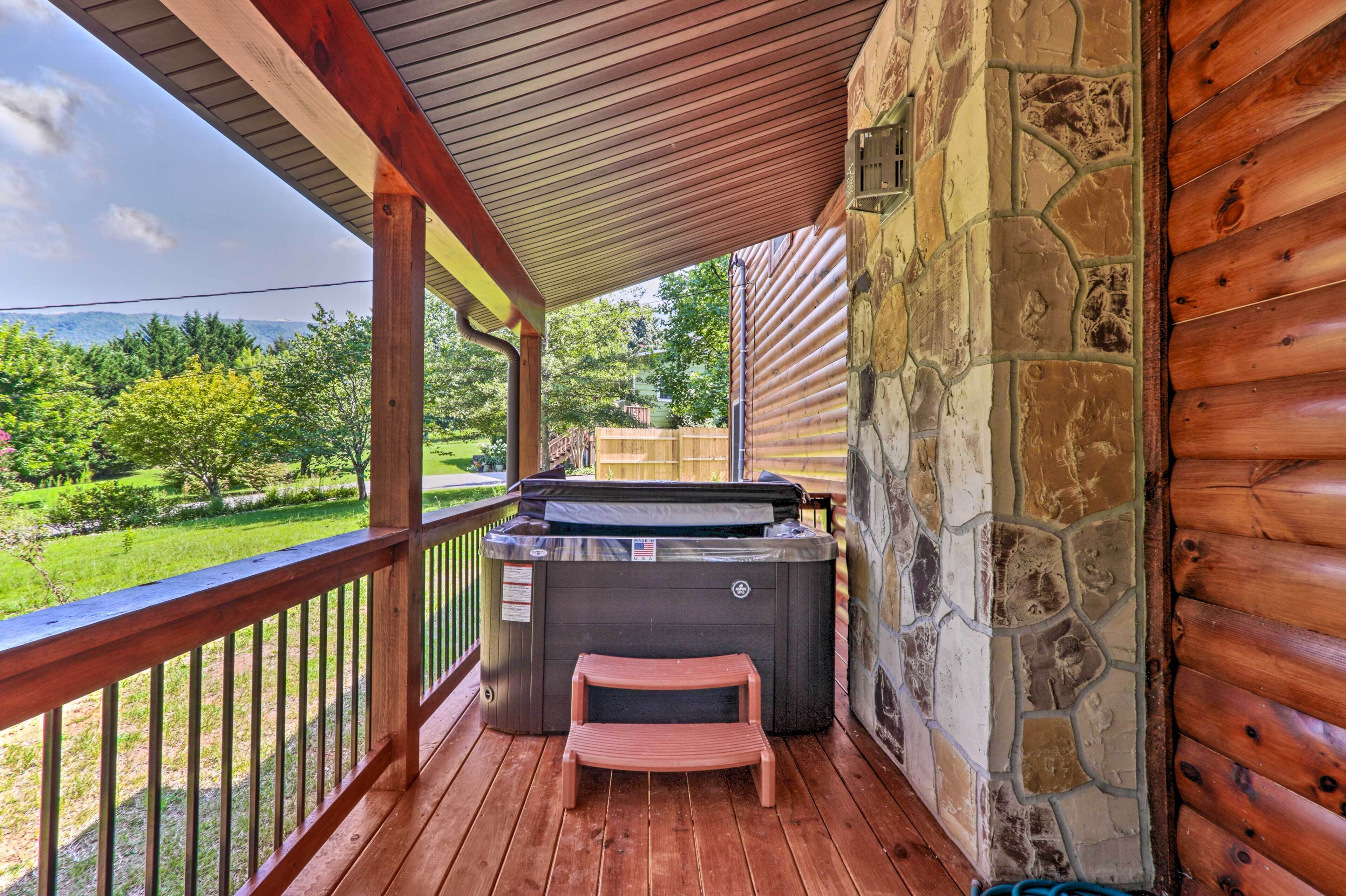 A wooden deck with a hot tub, stone wall, and a view of a green landscape.