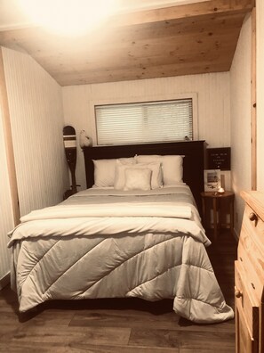 Een slaapkamer met een bed, een nachtkastje, een lamp en een raam met jaloezieën.