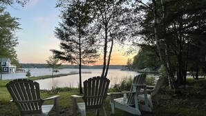 Kolme Adirondack-tyylistä puutarhatuolia, jotka on asetettu järven rannalle, ja taustalla näkyy talo.