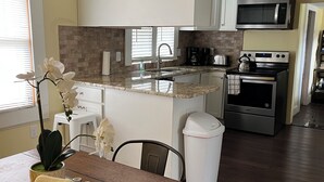 A modern kitchen with white cabinets, a granite countertop, a stainless steel stove, and a microwave. - Getaway Country Cottage - Entire house - Unique Find /Outdoor Decking           (New Bern)
