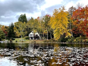 A lakeside house with a dock and a boat, surrounded by autumn-colored trees.
