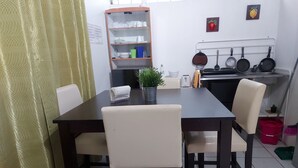 Uma sala de jantar com uma mesa, cadeiras, um vaso de planta e uma cozinha ao fundo.