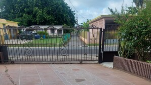 Uma área externa pavimentada com um portão de metal decorativo, um caminho de pedras e um jardim de rochas.
