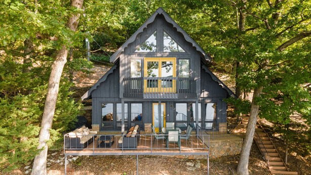Een chalet met balkon, grote ramen en een stenen fundering.