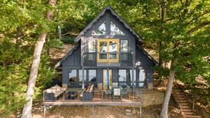 A cabin with a balcony, large windows, and a stone foundation.