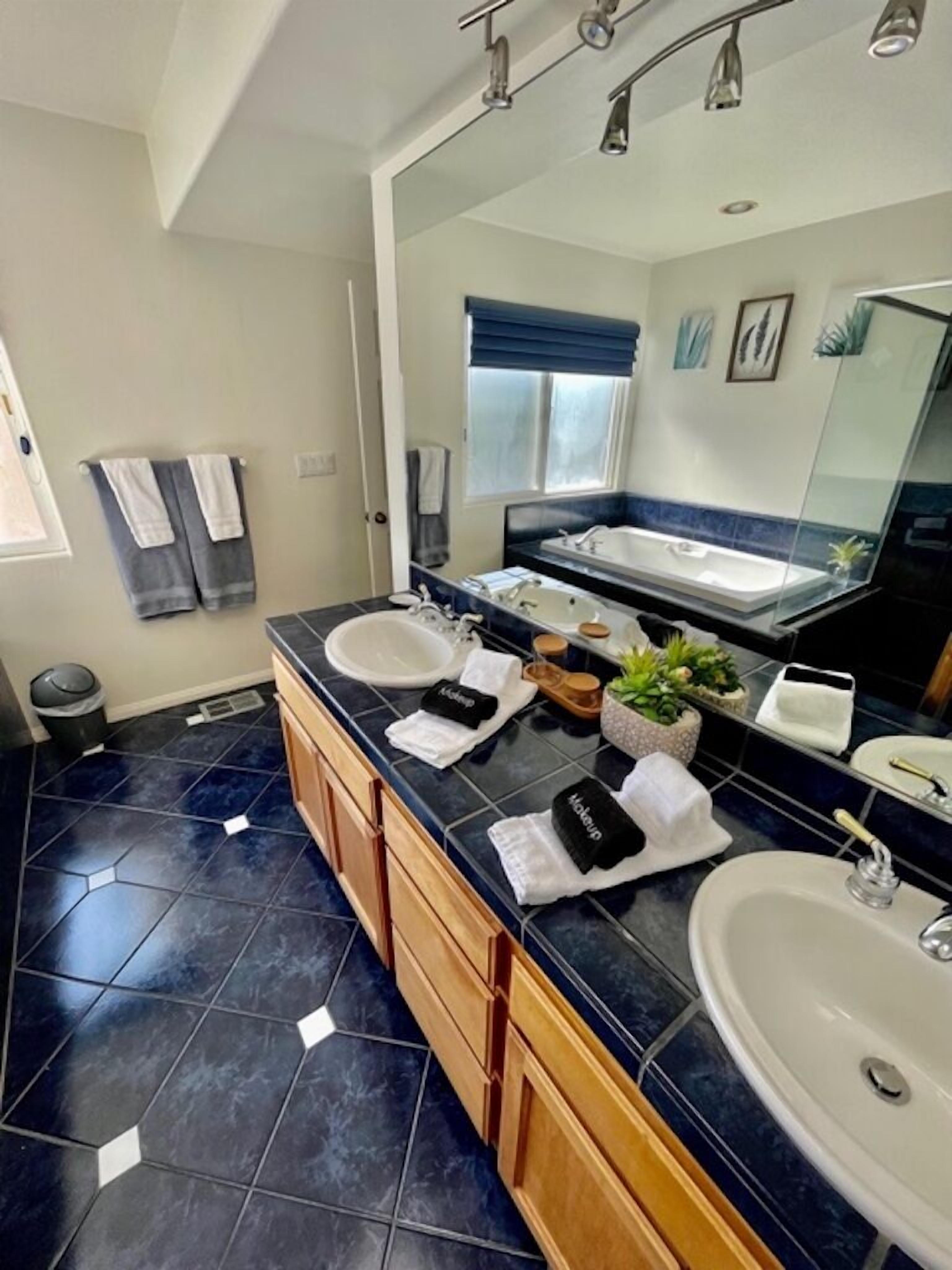 A modern bathroom with two sinks, a large mirror, and a bathtub.