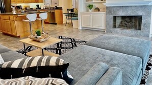 A modern living room with a grey sofa, a kitchen area with wooden cabinets, a dining area, and a fireplace. - Beautiful La Jolla Village Home, Sleeps 9 (La Jolla)