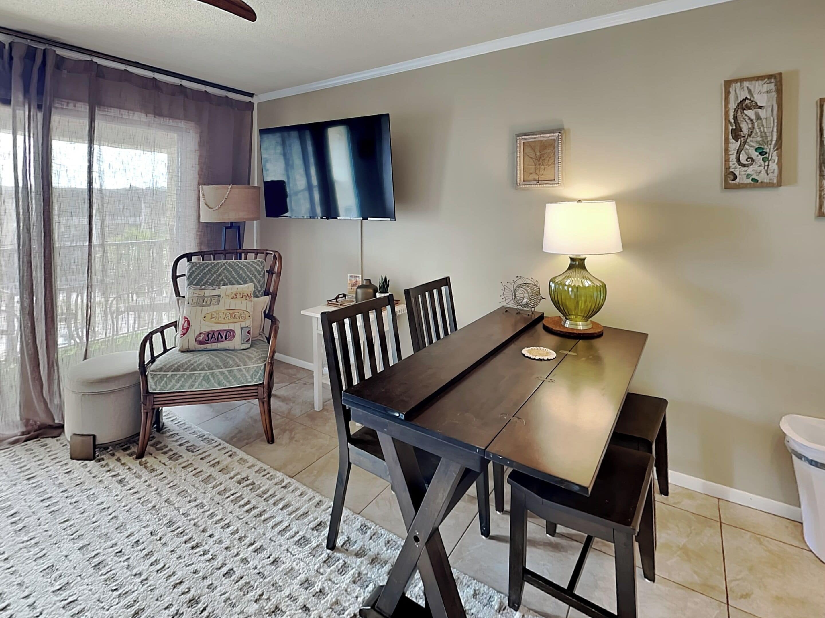 A dining area with a table, chairs, a TV mounted on the wall, and a lamp.