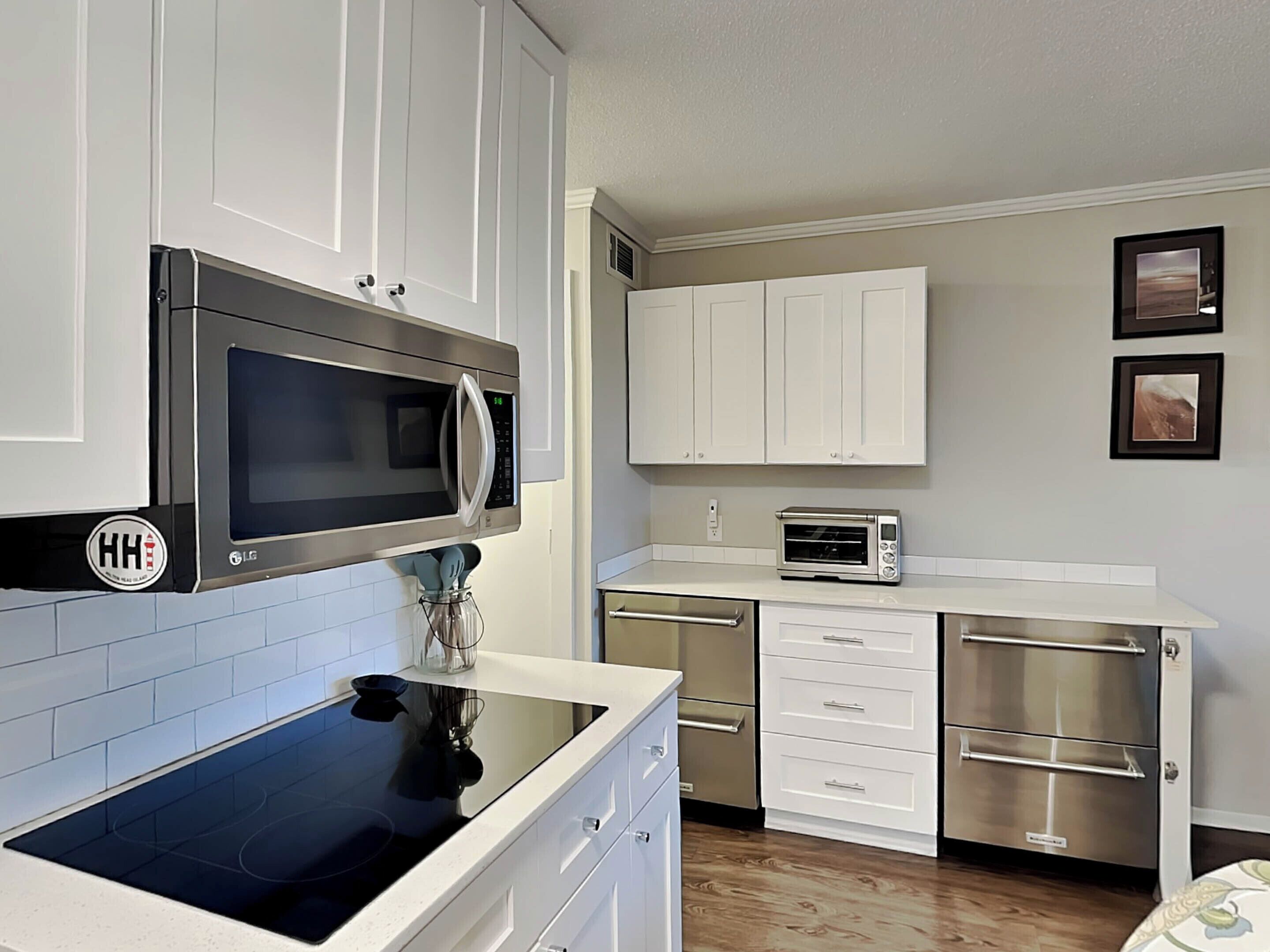 A modern kitchen with white cabinets, a black induction cooktop, stainless steel appliances, and a tiled backsplash.