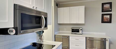A modern kitchen with white cabinets, a black induction cooktop, stainless steel appliances, and a tiled backsplash.