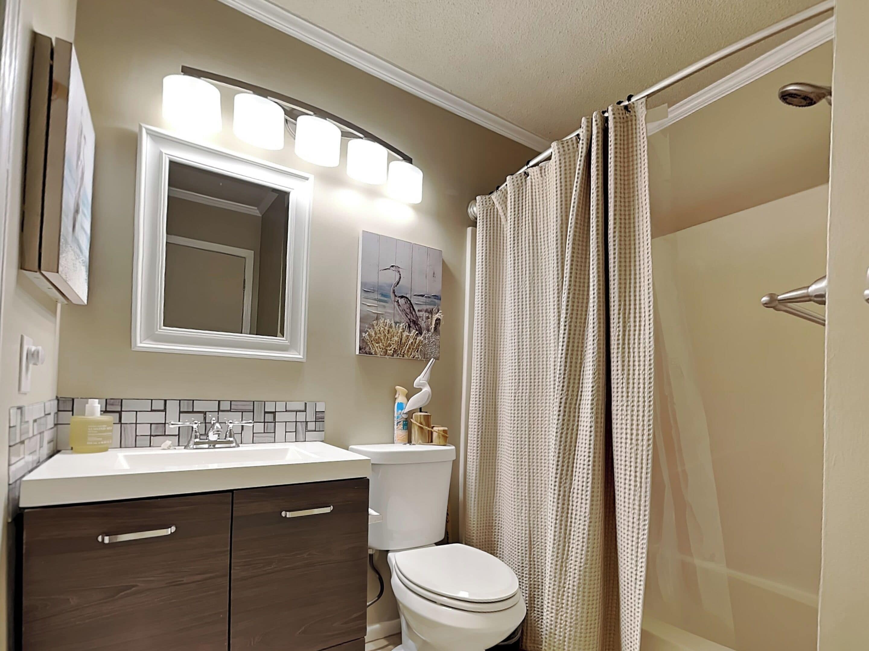 A bathroom with a white sink, dark wooden cabinets, a white toilet, a mirror, and a shower curtain.