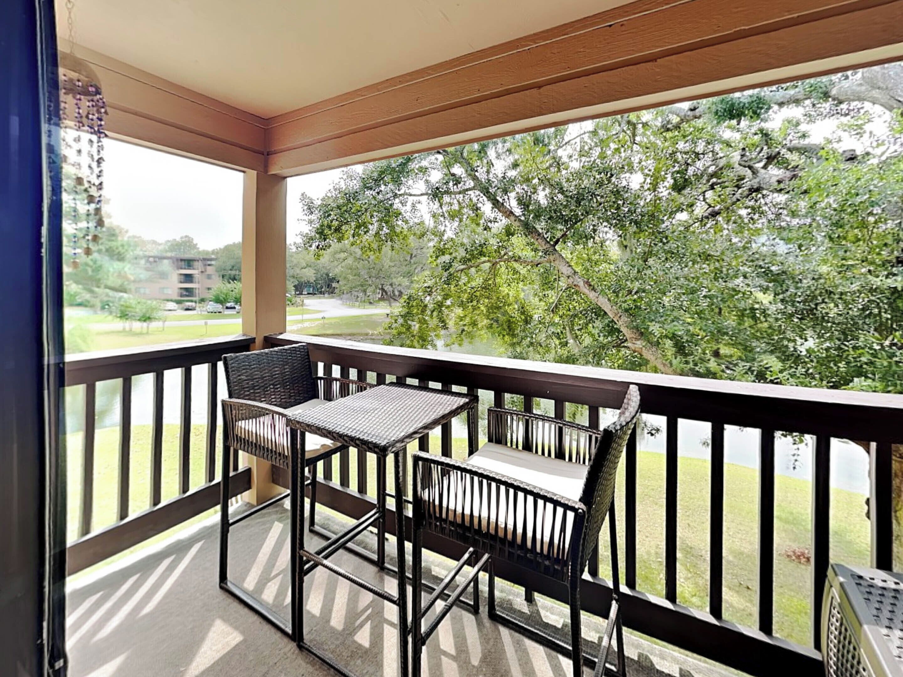 A balcony with two wicker chairs and a small table, overlooking a grassy area and trees.