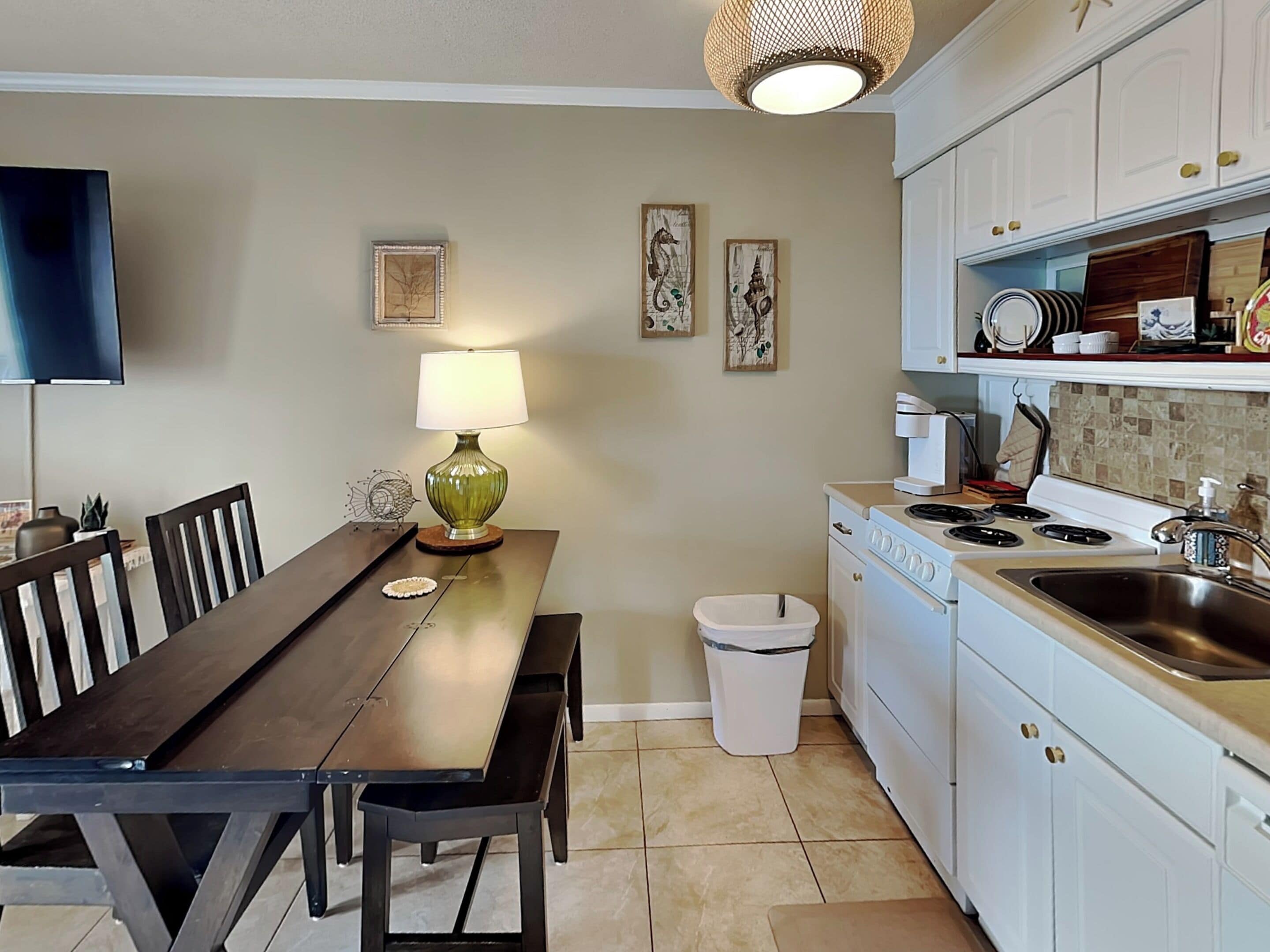 Cucina con mobili bianchi, piano cottura e lavello. C'è un tavolo da pranzo con sedie e una lampada.