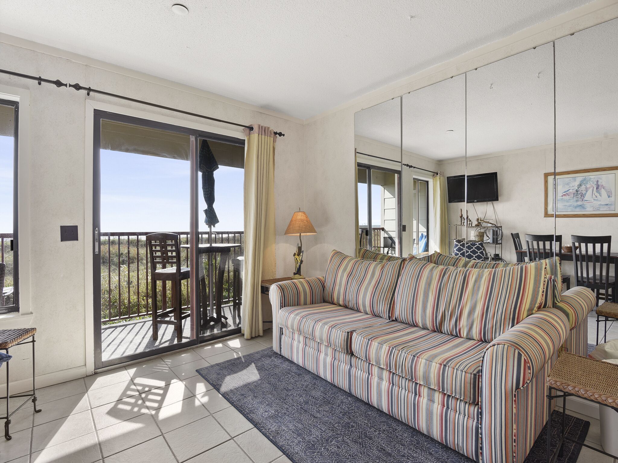A living room with a striped sofa, a table, chairs, a TV, and a balcony with a railing.
