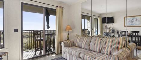 A living room with a striped sofa, a table, chairs, a TV, and a balcony with a railing.