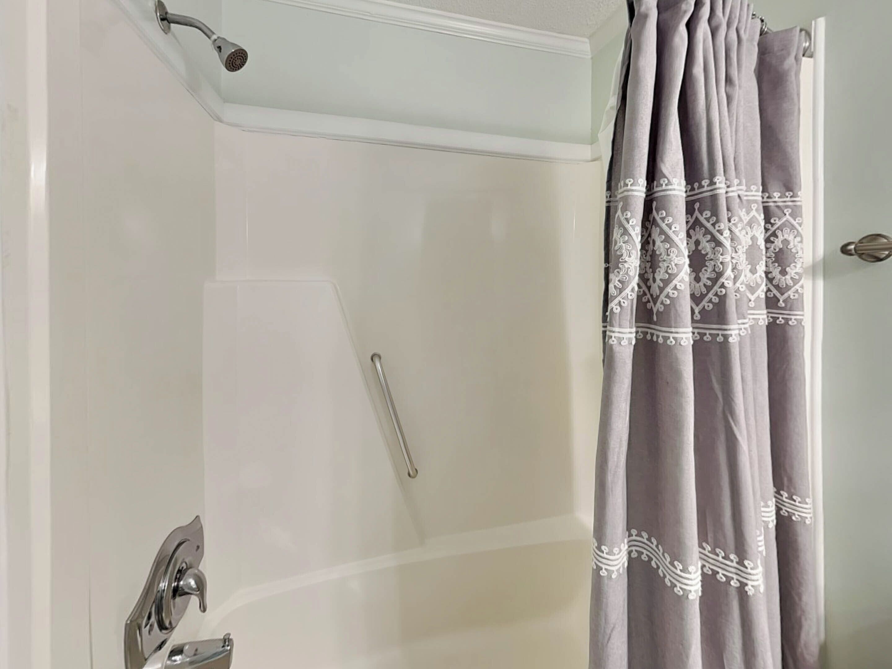A shower with a glass door, a showerhead, and a curtain with a pattern.