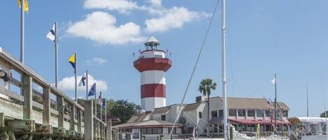 Un muelle con un faro, barcos y un edificio con varias banderas.
