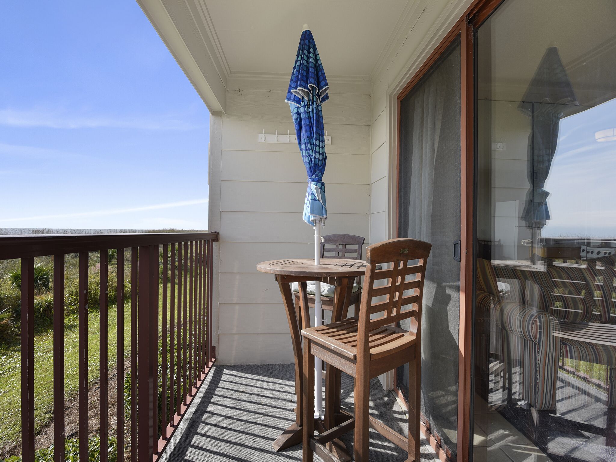 A balcony with a table and chairs, a blue umbrella, and a view of the landscape.