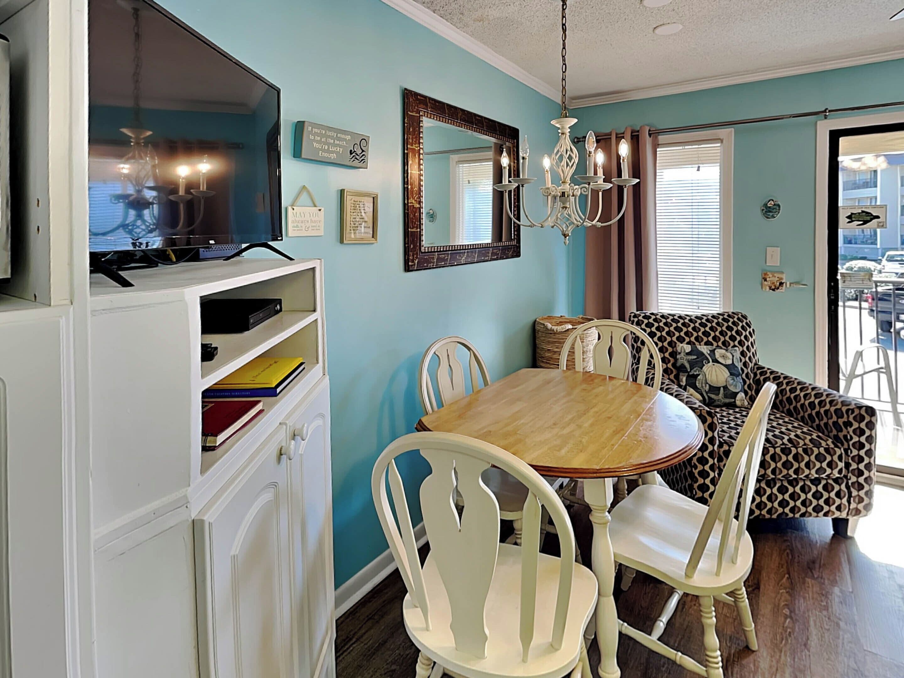 A dining area with a wooden table and white chairs, a television on a cabinet, and a chandelier.