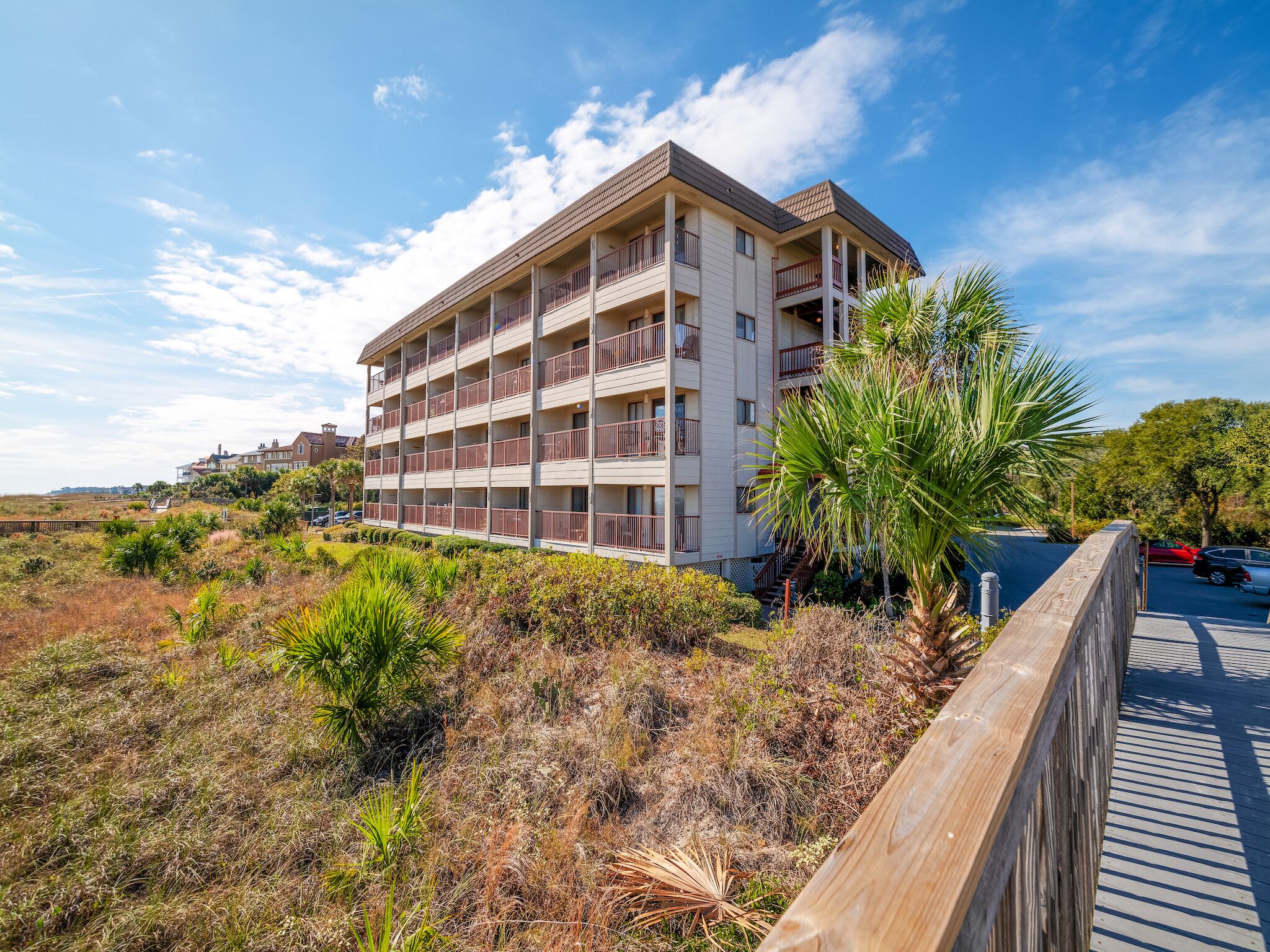 Um hotel com vários andares e varandas, localizado numa área costeira com vegetação seca e um calçadão de madeira.