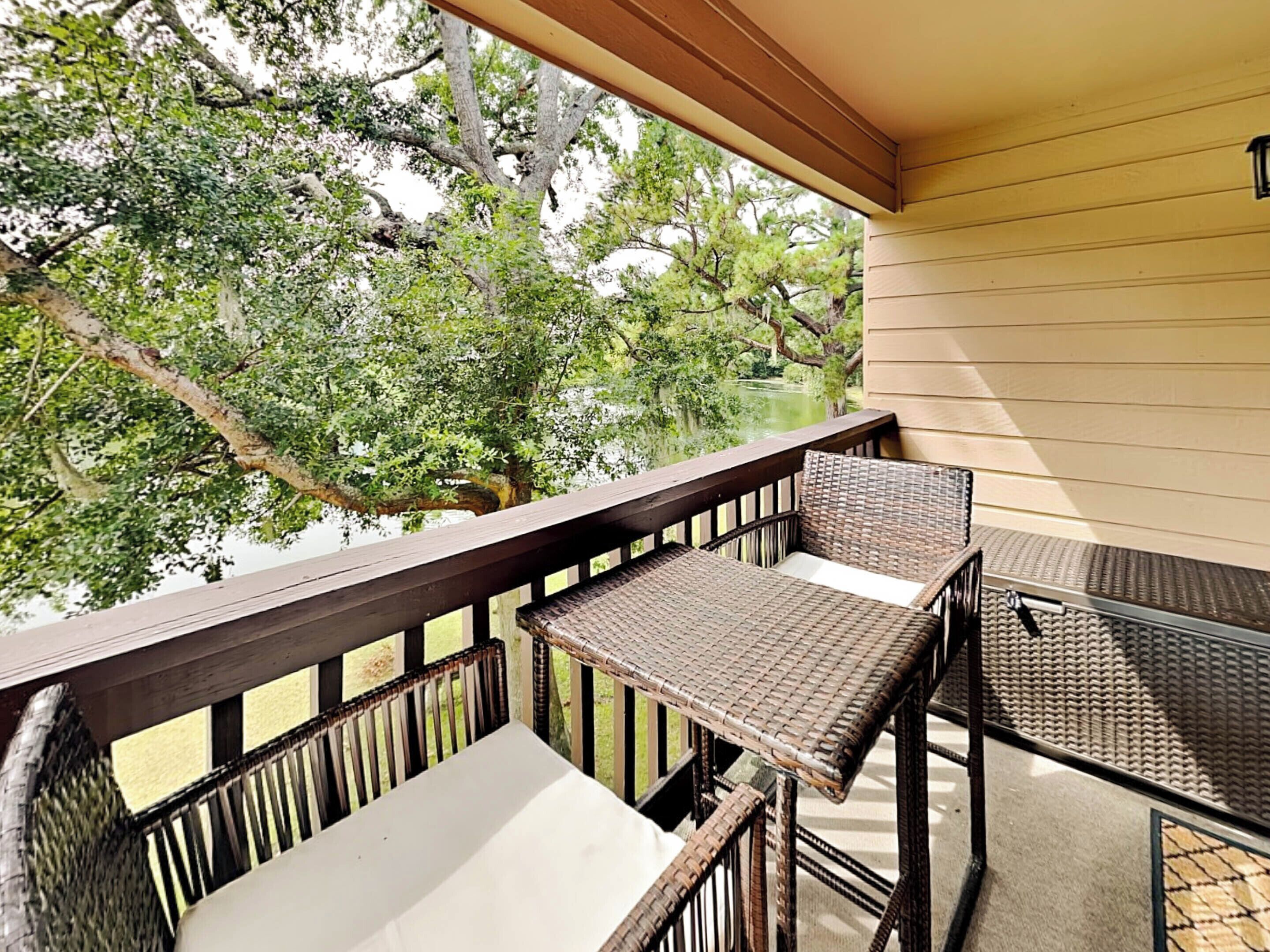 A balcony with wicker furniture, a view of trees and a body of water.