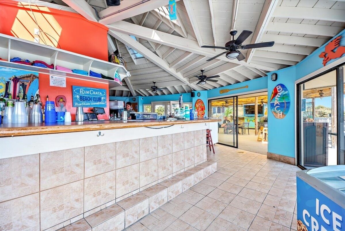 A beach club with a counter, ceiling fans, and an ice cream display.
