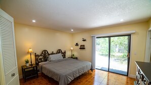 Een slaapkamer met een bed, nachtlampjes, een nachtkastje, een dressoir en een schuifdeur naar een terras.