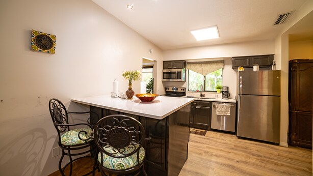 Een moderne keuken met een centraal eiland, donkere keukenkastjes, roestvrijstalen apparatuur en een eetgedeelte met twee stoelen.