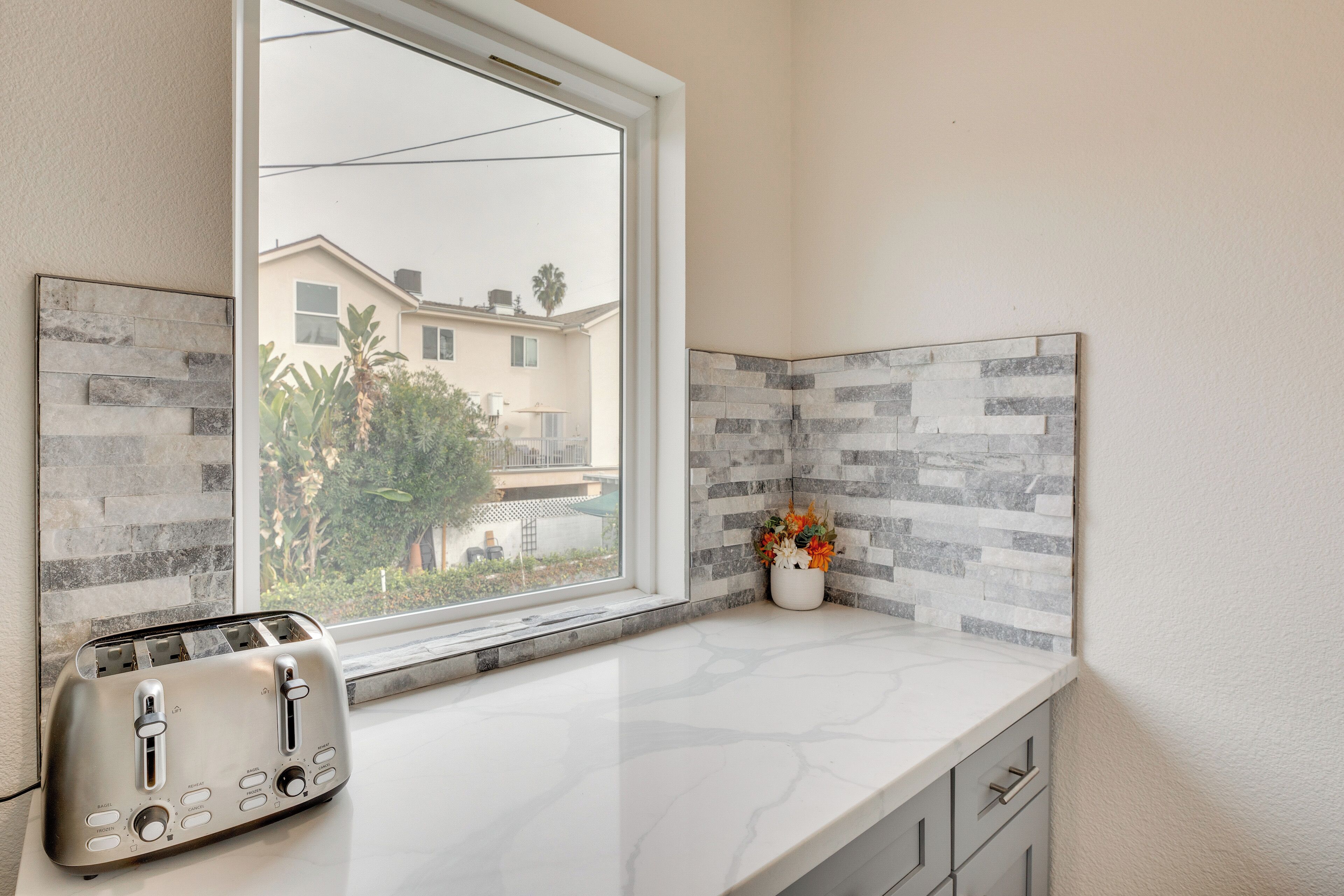 A kitchen with a built-in toaster, a window, and a backsplash with gray and white tiles.