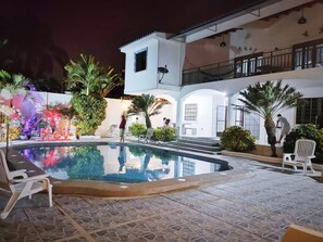 A pool area with a tiled floor, a small pool, and white lounge chairs.