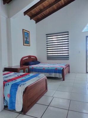A room with two wooden beds, a desk, a chair, a window with blinds, and a framed picture on the wall.