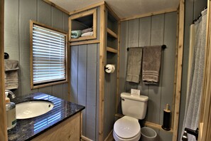 Ein Badezimmer mit einem Holzkosmetikschrank, einem Waschbecken, einer Toilette und einem Fenster mit Jalousien.