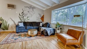 Een moderne woonkamer met een hoekbank, een salontafel en een groot raam met zonwering.