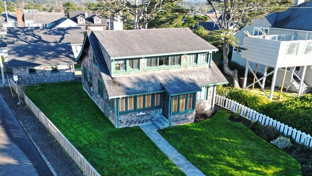 Uma casa de dois andares com telhado verde, varanda frontal e pequeno jardim da frente.