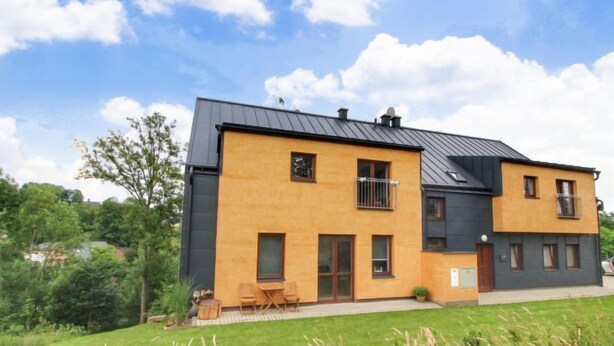 A two-story modern house with a flat roof, large windows, and a small balcony.