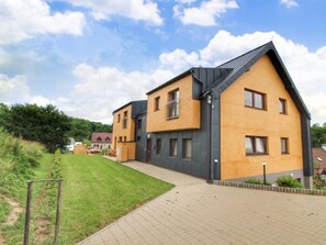 Un immeuble résidentiel moderne à deux étages, doté d’un toit en pente, de grandes fenêtres et d’une allée pavée.