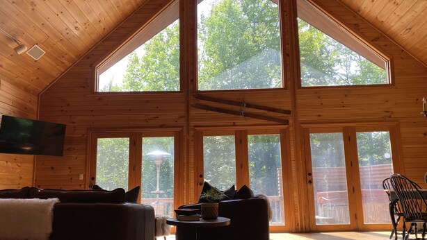 A spacious room with a high ceiling and large windows, a sofa, a table with a plant, and a TV mounted on the wall.