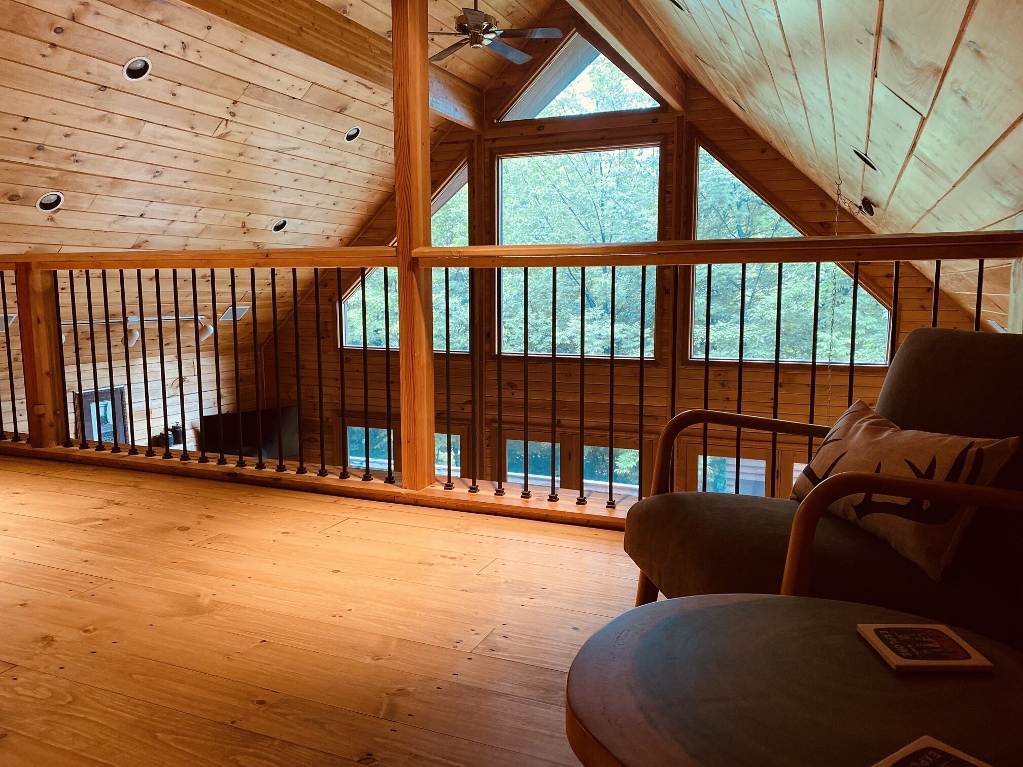 A wooden cabin interior with a balcony, wooden flooring, and large windows.
