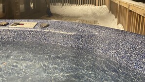 A hot tub with a wooden deck and snow accumulation around it.